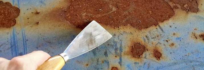 Hand mit Spachtel entfernt Rost